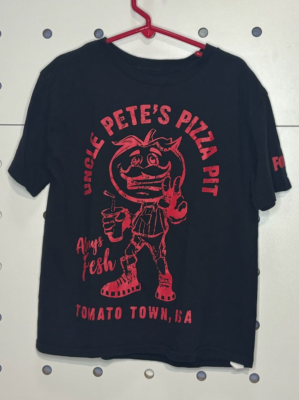 Black t-shirt with red graphic and text on a hanger against a pegboard background